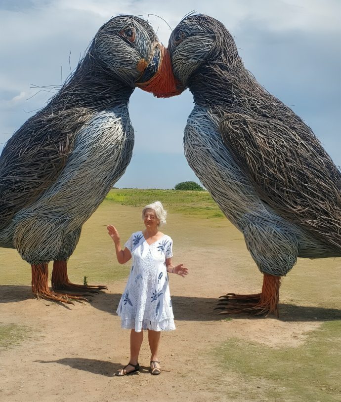 Woman standing between giant puffin sculptures.