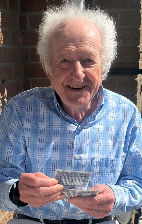 Elderly man smiling, holding playing cards.