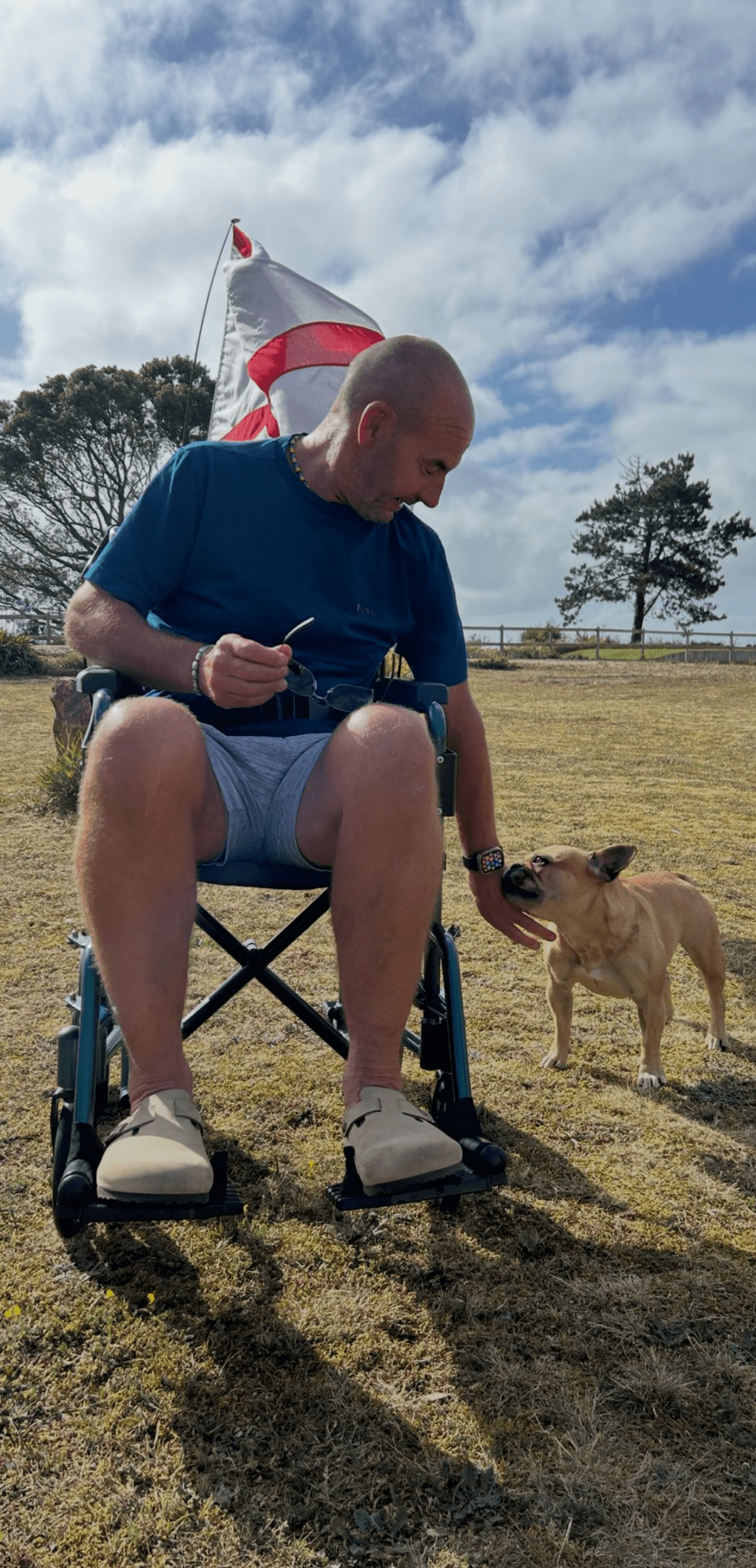 Man in wheelchair with dog outdoors.