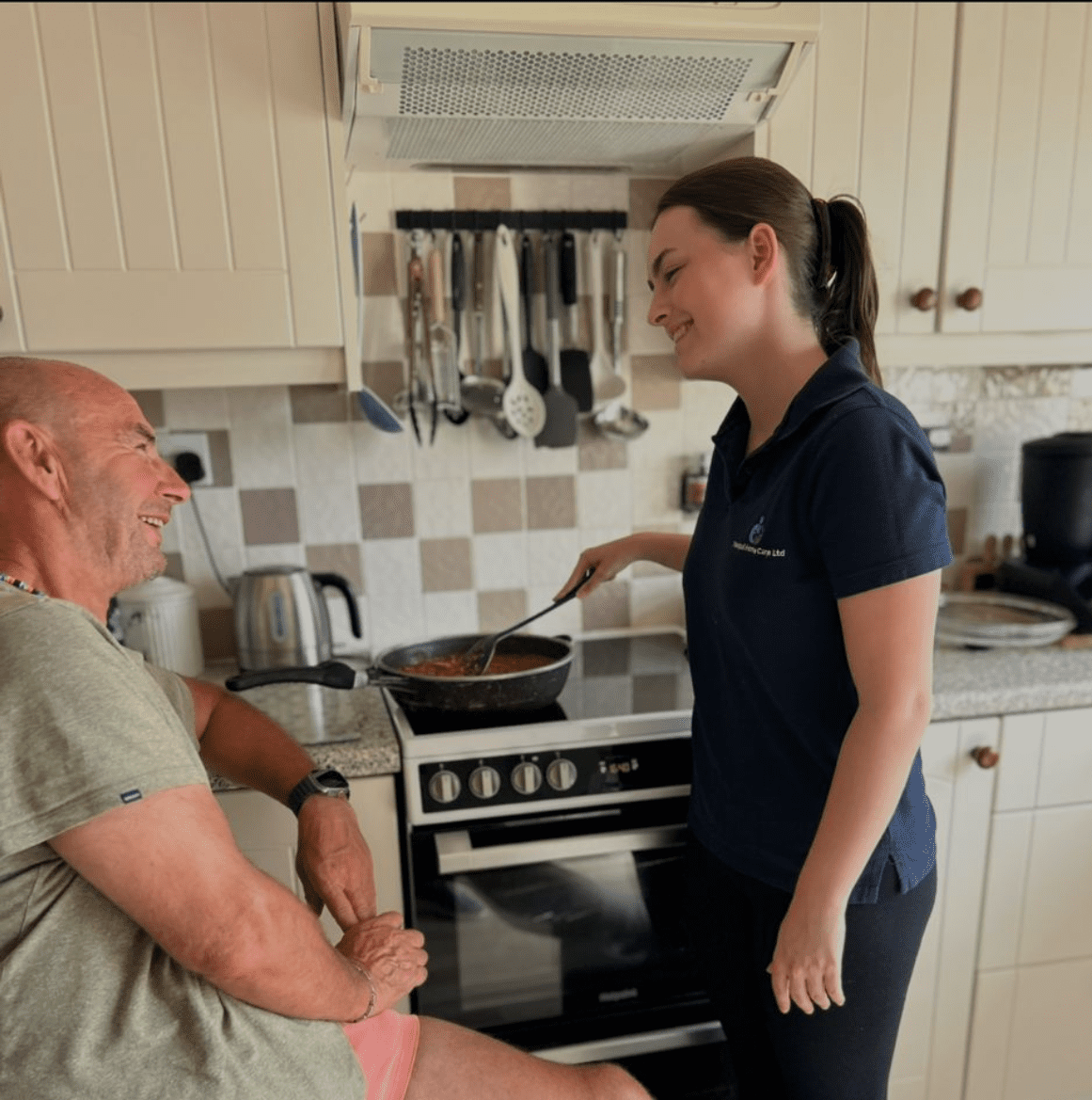 Woman cooking and chatting with seated man.
