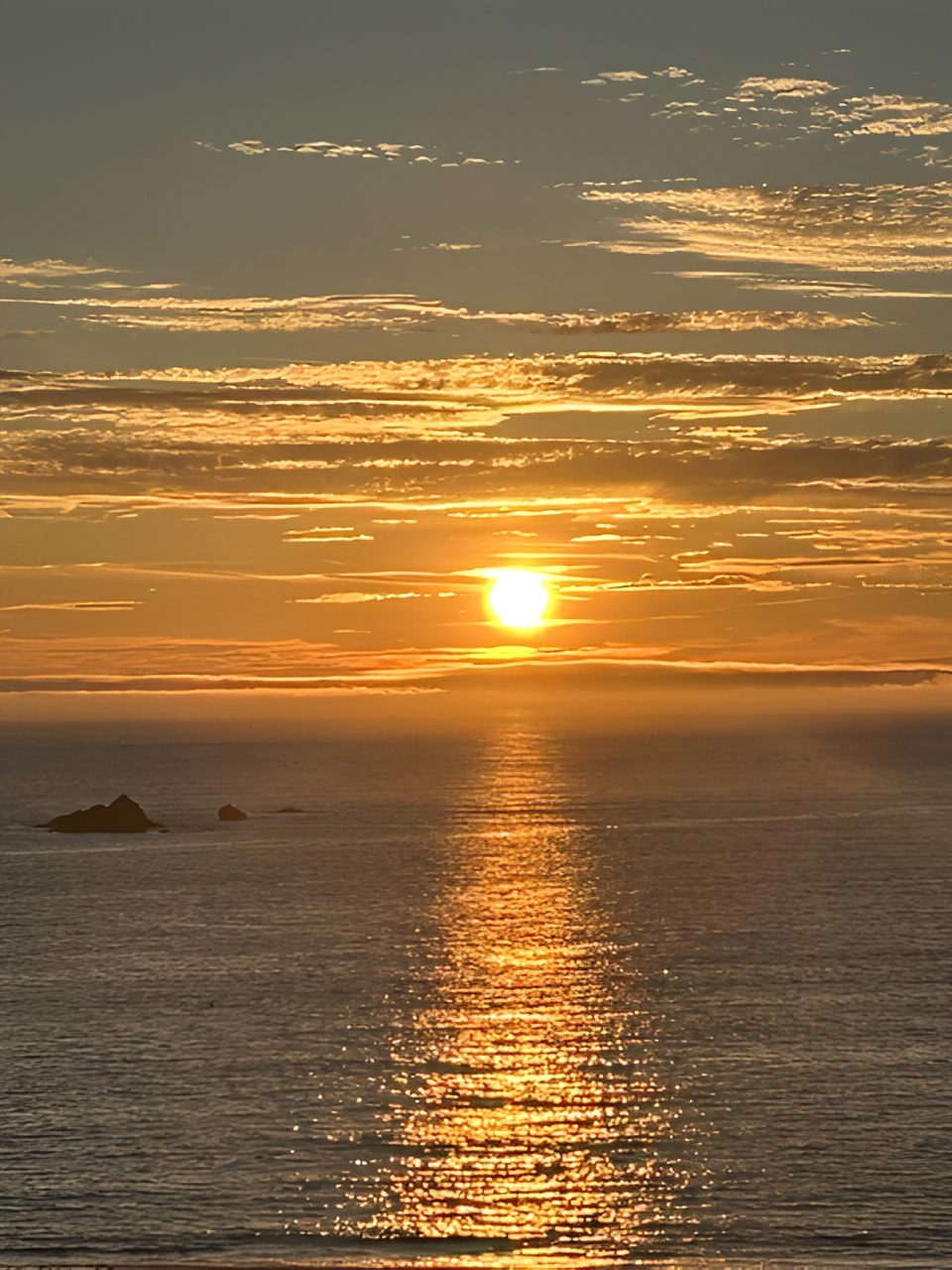 Sunset over ocean with scattered clouds.